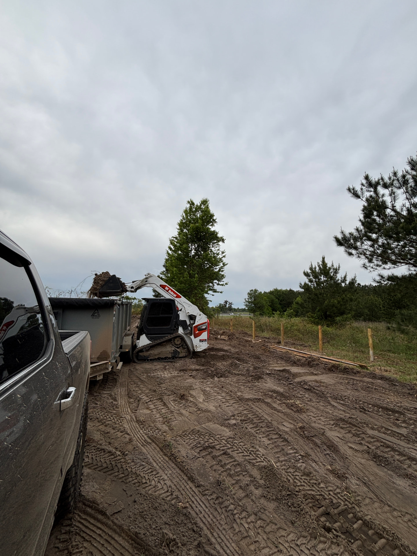 Bobcat skid steer loading dirt into a dump trailer on a clearing job