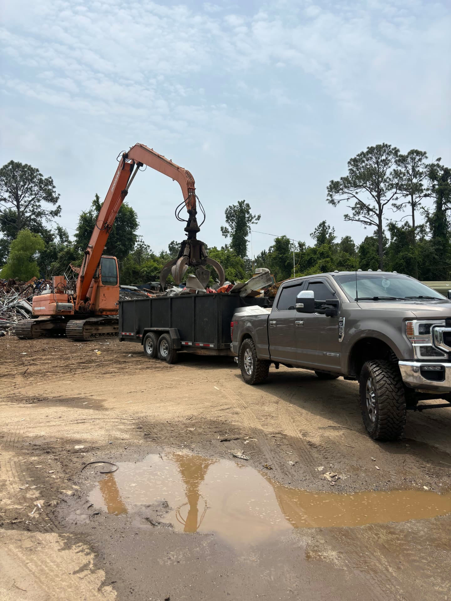 Excavator loading scrap metal into a dump trailer on a Frontier job site